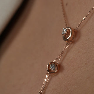 A close-up photo of a woman's neck wearing a delicate rose gold necklace adorned with two interconnected circles. This elegant piece is perfect for both casual and formal occasions, adding sophistication to any outfit. The image features the close-up front view of a swirling 14 KT Diamond Necklace, adorned with 0.21 carats of lab-grown diamonds, elegantly worn on the neck of the model of size 16 secured through a spring lock weighing a total of 3.28 grams