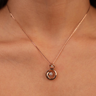 A view of a female pendant modelled on a neckline featuring a circular design in 14 KT rose gold. The pendant has an interlocking double circle motif, with one polished rose gold circle enveloping an inner circle set with pavé lab-grown diamonds totalling 0.26 carats and the product weight being 3.12 grams. The pendant hangs from a delicate rose gold cable chain necklace, allowing the intricate yet minimalist pendant to be showcased.