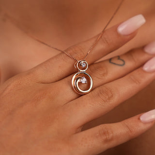 A view of an exquisite female pendant, modelled on a neckline, featuring a circular pendant crafted in 14 KT rose gold weighing 3.21 grams. The pendant displays an interlocking double circle design, with the outer rose gold circle elegantly embracing an inner circle pavé-set with shimmering lab-grown diamonds totalling 0.445 carats. This eternal knot motif is suspended from a delicate rose gold chain necklace, allowing a minimalist look.