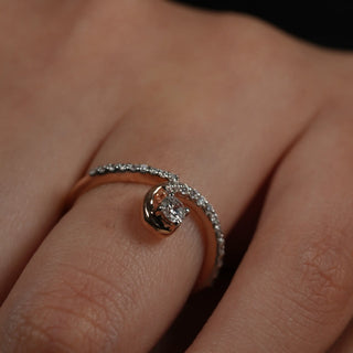 A front view of a ring of a size 12, on a model's hand, featuring an elegant infinity-inspired twist design in 14 KT rose gold. It showcases a graceful spiral shape encrusted with pavé-set lab-grown diamonds totalling 0.28 carats and the product weight being 2.41 grams. The twisted form creates a seamless and feminine look, while the rose gold metal provides a warm, flattering tone complemented by the brilliance of diamond accents.