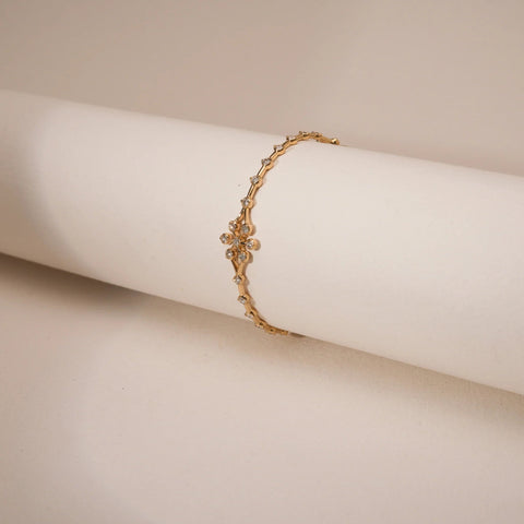The Golden Bud Trail Diamond Bangle, crafted in hallmarked 18 KT Yellow Gold with EF-VVS diamonds, reveals its intricate trail of golden buds and floral curves. A singular radiant centre stone anchors the design, embodying subtle grandeur in a lightweight, luxurious form.