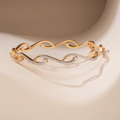 On a softly lit surface, this 14 KT yellow gold bangle showcases an open wave-like form accented with EF VVS round diamonds totaling 1.960 carats. Weighing 15.05 grams, the piece blends modern negative space with sparkling fluidity, making it a refined yet bold statement accessory