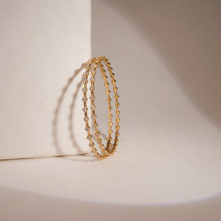 This is a classic yellow gold bangle size 2.5 features multiple lab grown diamonds of EF color and VVS clarity, totaling a 1.32 carats. The largest single stone measure 0.051, all balanced beutifully across totaling weight of 9.707 carats.The bangle is signature piece for those who appreciate elelvated minimalism.The twin bangle is frontal view against the badge background on a bangle holder highlights the elegance and minimilist approach of the bangle.