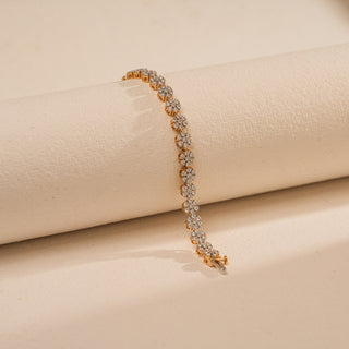 Single-strand Réia tennis bracelet featuring flower-inspired diamond clusters in a continuous gold design, draped over a textured ivory roll in warm light.