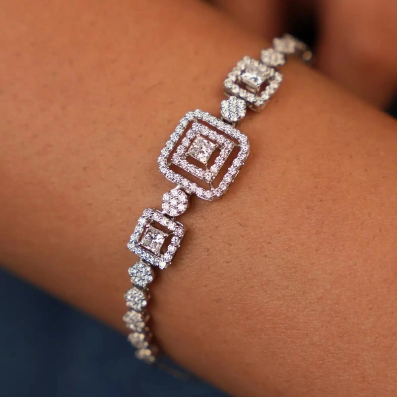 A close-up photo of a woman's wrist wearing a delicate bracelet with a series of interconnected diamond-studded squares. The bracelet features a larger square diamond in the centre, surrounded by smaller diamonds in a repeating pattern. The stunning view of the female bracelet of size 7 which weighs 5.51 grams is secured through a spring lock on the model’s hand showcases a pair of 14 KT white gold and the design made up of gold and lab-grown diamond of 2.041 carats