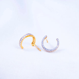 Half-hoop stud earrings lined with small round diamonds in a curved open design, placed on a soft white textured fabric background.