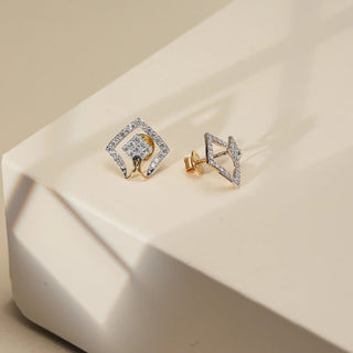 Set against a softly shadowed beige surface, a pair of 14 KT yellow gold diamond stud earrings is displayed in a symmetrical front view. The design features a striking dual-layered diamond silhouette, an inner and outer diamond shape encrusted with EF-color, VVS-clarity round diamonds totalling 0.580 carats. Weighing 2.789 grams gross and 2.673 grams net, these earrings blend geometric artistry with luxurious brilliance.