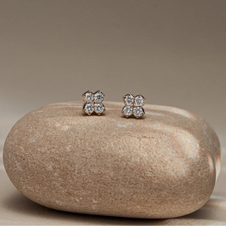 Front view of Reia's Diamond Cluster Flower Stud Earrings on a smooth beige stone, showcasing the four-petal floral silhouette in 18KT yellow gold. Set with EF-VVS round lab-grown diamonds, the studs radiate soft brilliance, perfect for daily wear or gifting.