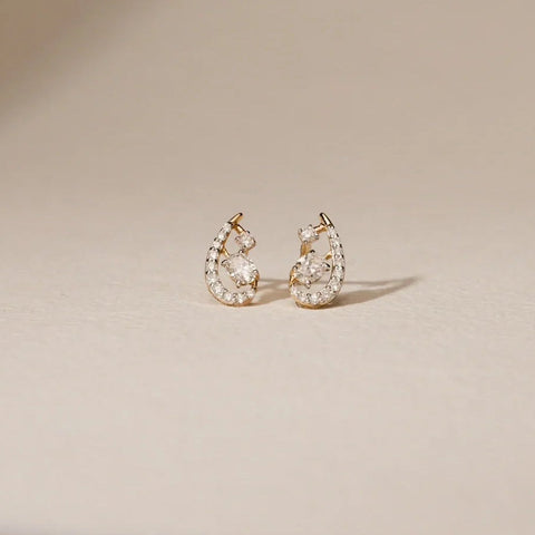 A pair of elegant 14 KT yellow gold stud earrings, gross weight 1.43g, featuring a central cluster of brilliant round EF VVS diamonds totaling 0.190 carats, arranged in a subtle floral design. The earrings are displayed on a subtly textured dark surface, with soft lighting emphasizing their intricate pattern and continuous sparkle.