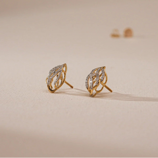 Side profile of Reia's Twisted Flame Diamond Stud Earrings on a cream surface, highlighting the bold, twisted gold design and the subtle dome of diamond clusters. A modern yet timeless pair crafted for sparkle and strength.