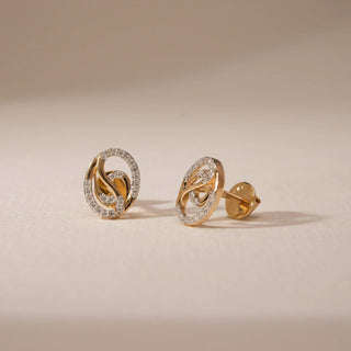 A pair of dazzling 14 KT yellow gold stud earrings, gross weight 2.124g, designed with a prominent floral motif and adorned with 0.210 carats of round EF VVS diamonds. The earrings are presented on a textured dark surface, with a blurred background, drawing focus to their intricate design and luminous diamond arrangement.