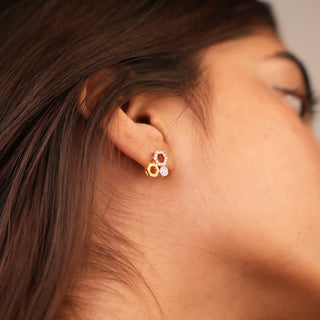 A side view of a pair of three-tone female stud earrings secured with a bombay screw, modelled on an earlobe, with an interlocking geometric design. The earrings are crafted from 14 KT multi colour gold (yellow, white, and rose gold) and feature lab-grown diamonds totalling 0.49 carats set in a pavé style with a total weight of 3.08 grams. The interlocking circles form an infinity symbol motif, creating an elegant and timeless look.