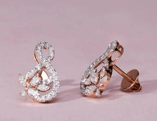 A pair of elegant 18 KT rose gold drop earrings, gross weight 3.1g, each featuring a captivating cluster of brilliant marquise-shaped EF VVS diamonds, totaling 0.730 carats per pair, forming an elaborate, elongated design. The earrings are displayed on a light beige textured surface, casting subtle shadows, highlighting their detailed craftsmanship and sparkling elegance