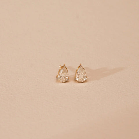 A pair of exquisite 18 KT yellow gold stud earrings, gross weight 2.23g, each featuring a large pear-shaped cluster meticulously set with brilliant round EF VVS diamonds, totaling 1.480 carats. The earrings are angled on a soft, dark textured surface, with a subtle circular pattern and a blurred background, emphasizing their opulent sparkle and intricate design