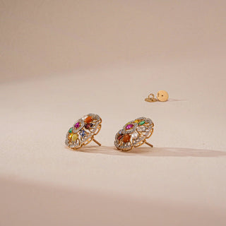 Side profile of Reia's Nine-Gem Halo Heritage Earrings resting on a beige background, revealing the intricate Bombay screw setting and elegant tri-gold framework supporting the gemstone cluster. The fine craftsmanship and structural depth evoke heritage and modern refinement.