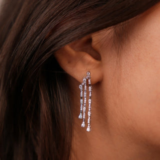 A close-up front view of an female earring weighing a total of 6.49 grams push-pull screw mechanism, modelled on an earlobe, crafted in a long, dangling style made of 14 KT white gold with multiple lab grown diamond-shaped gemstones totalling 0.84 carats. The design features a linear cascade of these diamond-shaped stones suspended elegantly, creating a sleek and sparkling drop earring.