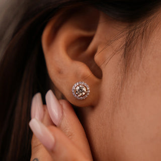 A close-up view of an exquisite female stud earrings crafted in 14 KT yellow gold secured through a bombay screw with a total weight of 4.4403 grams, on a model, featuring a stunning round brilliant-cut lab-grown diamond, totalling 1.116 carats with a solitaire of 0.45 carats The halo design adds a radiant sparkle, enhancing the fire and brilliance of the centre diamonds.