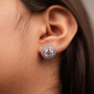 A front view of a pair of elegant female earrings and has a total weight of 5 grams secured through a bombay screw, on a white background, crafted in 18 KT white gold. The earrings feature an round-shaped lab-grown diamond drop, totalling 3.849 carats, suspended from a diamond-encrusted hoop with a pavé setting. The design combines the brilliance of the diamond drops with the sparkling diamond-lined hoops, creating a luxurious and timeless look.