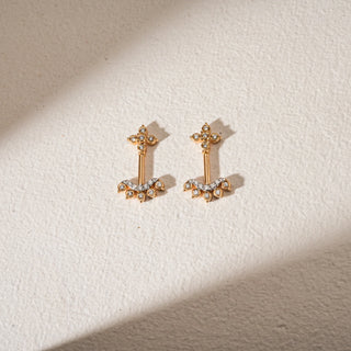 Front view of Reia's Temple Crest Diamond Studded Koppu displayed on a beige background. The design features floral diamond motifs and a vertical bar in 18KT yellow gold, adorned with EF VVS round lab grown diamonds totaling 0.280 carats. The intricate detailing and symmetrical silhouette evoke traditional temple-inspired craftsmanship.