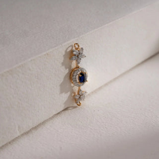 A delicate 18 KT yellow gold pendant, gross weight 1.973g, featuring a central round gemstone of 0.39 carats, framed by a halo of brilliant round EF VVS diamonds totaling 0.500 carats. The pendant hangs from a fine chain and is displayed on a soft, light beige textured surface, casting a subtle shadow, with a blurred light background, emphasizing its elegant design and sparkling gems