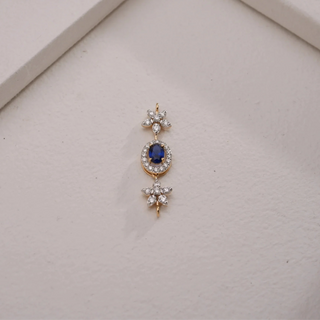 A radiant 18 KT yellow gold pendant, gross weight 1.973g, featuring a central 0.39 carat round gemstone surrounded by a halo of 0.500 carats of round EF VVS diamonds. The pendant is presented with its chain draped gracefully on a light brown textured surface, with a blurred background, drawing focus to its vibrant centerpiece and sparkling diamond frame.