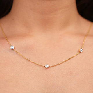 A close-up photo of a woman's neck wearing a delicate yellow gold necklace adorned with three round-cut diamonds. The diamonds are evenly spaced along the chain, creating a timeless and elegant design.  The combination of yellow gold and diamonds creates a versatile look, making this necklace a valuable addition to any jewellery collection. The image showcases the front view of a 0.7 carat Lab Grown Diamond female Necklace of size 16, secured with a spring lock crafted in 14 KT Yellow Gold.