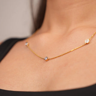 A close-up photo of a woman's side neck wearing a delicate yellow gold necklace adorned with three round-cut diamonds. The diamonds are evenly spaced along the chain, creating a timeless design. The combination of yellow gold and diamonds creates a versatile and timeless look, making this necklace a valuable addition to any jewellery collection. The image showcases the front view of a 0.7 carat Lab Grown Diamond female Necklace of size 16, secured with a spring lock crafted in 14 KT Yellow Gold