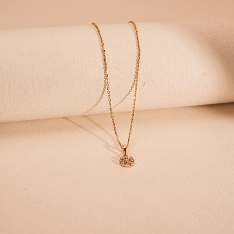 An elegant 18 KT yellow gold necklace, with a gross weight of 3.095 grams, is displayed horizontally across the center of a smooth, light beige background. The delicate chain leads to a circular pendant adorned with sparkling round VVS EF diamonds, totaling 0.100 carats, arranged in a subtle cluster around a central element.