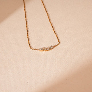 This exquisite 14 KT yellow gold necklace, weighing 2.176 grams gross, is presented with its diamond-studded rectangular bar pendant positioned in the lower right section of a subtly textured, light peach-toned surface. The pendant features brilliant emerald-cut VVS EF diamonds, totaling 0.940 carats, emphasizing its minimalist and modern design.