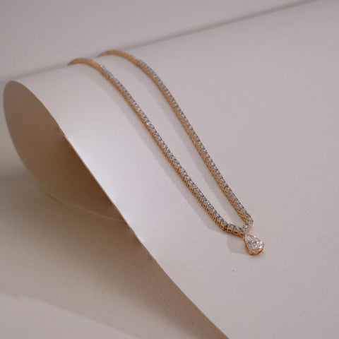 A luxurious 18 KT Yellow gold necklace, gross weight 18.993g, featuring a central cluster of brilliant pear-shaped EF VVS diamonds, totaling 4.005 carats, arranged in a dazzling, flowing design. The necklace is gracefully curved and displayed on a soft, light beige textured surface, with a subtle shadow and a blurred background, emphasizing its intricate detail and spectacular sparkle.