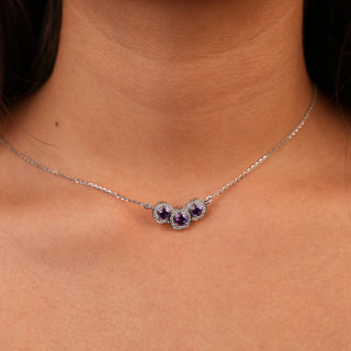 Front view of a Lab Grown Diamond female Necklace crafted in 14 KT White Gold, featuring 0.28 carats of diamonds and a total weight being 5.35 grams. The necklace presents a delicate chain adorned with three round-cut purple gemstones, presumably amethysts, arranged in a descending triangle pattern. Each gemstone is encircled by a halo of smaller, sparkling diamonds, enhancing their brilliance on a model."