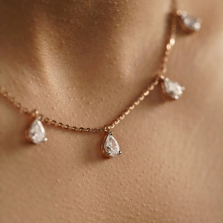 Side view of a delicate 14 KT rose gold female chain adorned with five pear-shaped Lab Grown diamonds, totalling 2.16 Carats with a solitaire of 0.50 carats with size 16 and the weight of the product is 4.75 grams with EF-VVS clarity with a fish lock to keep the necklace secured. The diamonds hang gracefully in a staggered, V-shaped pattern against a model's neck.