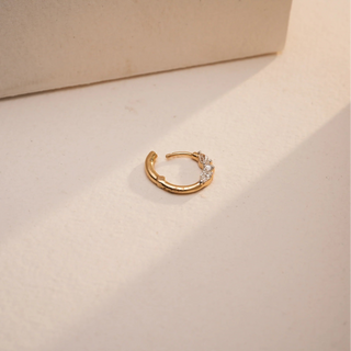 The 18KT yellow gold Reia nose pin quietly settles down on a textured neutral surface showcasing three pear shaped diamonds in graduated sizes with EF color, VVS clarity.  The total diamond weight is 0.140 carats.  The design radiates soft brilliance in a lightweight, everyday nose pin.