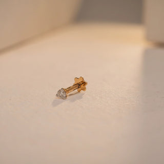 Side view of the Lustre Single-stone Nosepin by Réia, crafted in 18 KT yellow gold and displayed on a softly lit, textured surface with warm highlights. The design features a single round lab-grown diamond set in a minimalist gold frame with a South screw-back closure. The diamond weighs 0.04 carats and exhibits EF color and VVS clarity, emphasising subtle brilliance and everyday elegance.