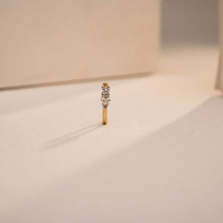 Standing upright on a textured cream backdrop, this Reia hanging nose pin showcases a vertical trio of EF color, VVS clarity lab grown diamonds, including a pear-cut centerpiece. Crafted in 14KT yellow gold, it reflects minimal charm with brilliant detailing.