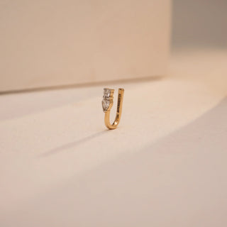 This elegant U-shaped nose pin by Reia is crafted in 14KT yellow gold and adorned with 0.070 carats of VVS clarity, EF color lab grown diamonds. Viewed from the side, the pear-cut stone adds a soft curve of brilliance under a warm-toned spotlight.