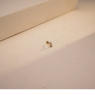 A close-up view of a radiant 14 KT yellow gold nose pin, weighing 0.325g, showcasing its prominent 0.080 carat luminous round EF VVS diamond and south screw. The nose pin is positioned on a light beige textured fabric, creating soft shadows, with a blurred light background, highlighting its detailed craftsmanship and continuous brilliance.