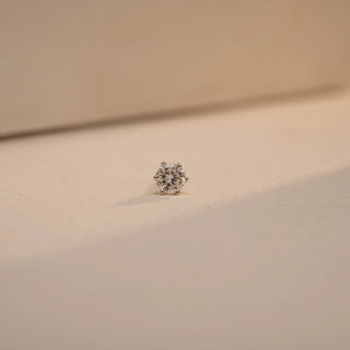 A gorgeous Reia solitaire nose pin with a 0.150 carat round lab grown diamond of EF color and VVS clarity. Set in a classic six prong mount, the diamond sparkles from a clear beige background, under soft directional lighting - bringing to you timeless elegance in a minimal form.