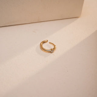 This delicate Reia nose pin in 14KT yellow gold lies flat on a warm beige surface, lit by natural light. The 0.04 carat round EF color, VVS clarity lab grown diamond glows at the center, creating a modern, effortless look with its push & pull setting and refined shape.