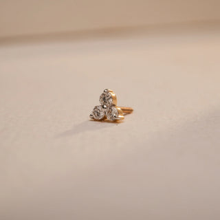 A close-up view of a delicate 14 KT yellow gold nose pin, weighing 0.253g, showcasing its prominent 0.060 carat luminous round EF VVS diamond. The nose pin is positioned on a light beige textured fabric, creating soft shadows, with a blurred light background, highlighting its detailed craftsmanship and continuous brilliance.