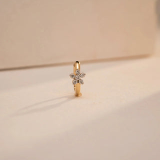 A 14KT yellow gold nose pin stands upright, showcasing a delicate floral diamond motif at the center, with six round lab grown diamonds arranged like petals. The soft lighting casts a natural shadow, emphasizing its intricate design and shine