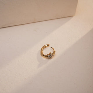 A top-down view of the floral diamond nose pin, slightly open, reveals the push & pull mechanism. The diamond flower detail is clearly visible, resting on a matte ivory surface with directional light adding depth and shadow.