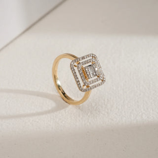 Regal Geometry Cocktail Diamond Ring in 18KT Yellow Gold, featuring concentric square frames of baguette and round-cut diamonds, photographed at an angled side view on a soft beige surface with natural shadows.