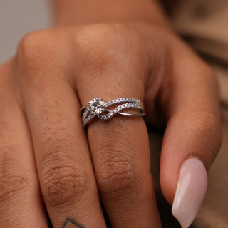 A close-up top of a female ring of size 12, on a model, showcasing a contemporary twist design with intertwining diamond-encrusted bands surrounding a brilliant round centre lab-grown diamond. Crafted in 14 KT white gold, the total diamond carat weight is 0.73 carats with a solitaire of 0.45 carats and the weight of the product is 3.28 grams, creating a dazzling and intricate look. The split shank style adds an elegant, free-flowing appearance.