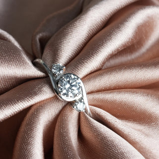 On a velvet cloth, A close-up top of a female ring of size 12, on a model, showcasing a contemporary twist design with an intertwining diamond of a trinity. Crafted in 14 KT white gold, the total diamond carat weight is 0.65 carats with a solitaire of 0.51 carats and the weight of the product is 2.15 grams, creating a dazzling and intricate look