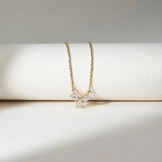 Top view of Three Stone Diamond Pendant Necklace in 14KT Yellow Gold, featuring two emerald-cut lab grown diamonds with a pear-shaped drop below. Placed on a beige backdrop, the design highlights modern elegance and sparkle.
