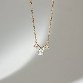 Front view of Three Stone Diamond Pendant Necklace in 14KT Yellow Gold, featuring two emerald-cut lab grown diamonds with a pear-shaped centre in prong setting. Set on a neutral backdrop, the design highlights brilliance and symmetry.
