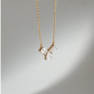 Angled view of Three Stone Diamond Pendant Necklace in 14KT Yellow Gold, featuring two emerald-cut lab grown diamonds with a pear-shaped centre in prong setting. Set on a neutral backdrop, the design highlights depth and brilliance.
