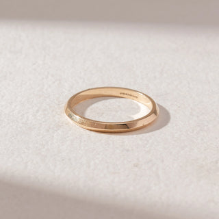 Top view of Minimal Faceted Band Ring in 14KT Yellow Gold, featuring a slim geometric profile with polished facets. Set on a soft beige surface, the design reflects clean lines and subtle shine.
