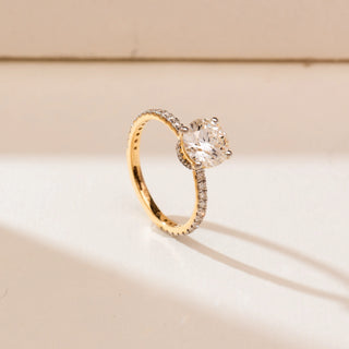 Side angle view of 14KT yellow gold ring featuring a round brilliant-cut centre diamond in a prong setting with a slender pavé-set band of round diamonds.